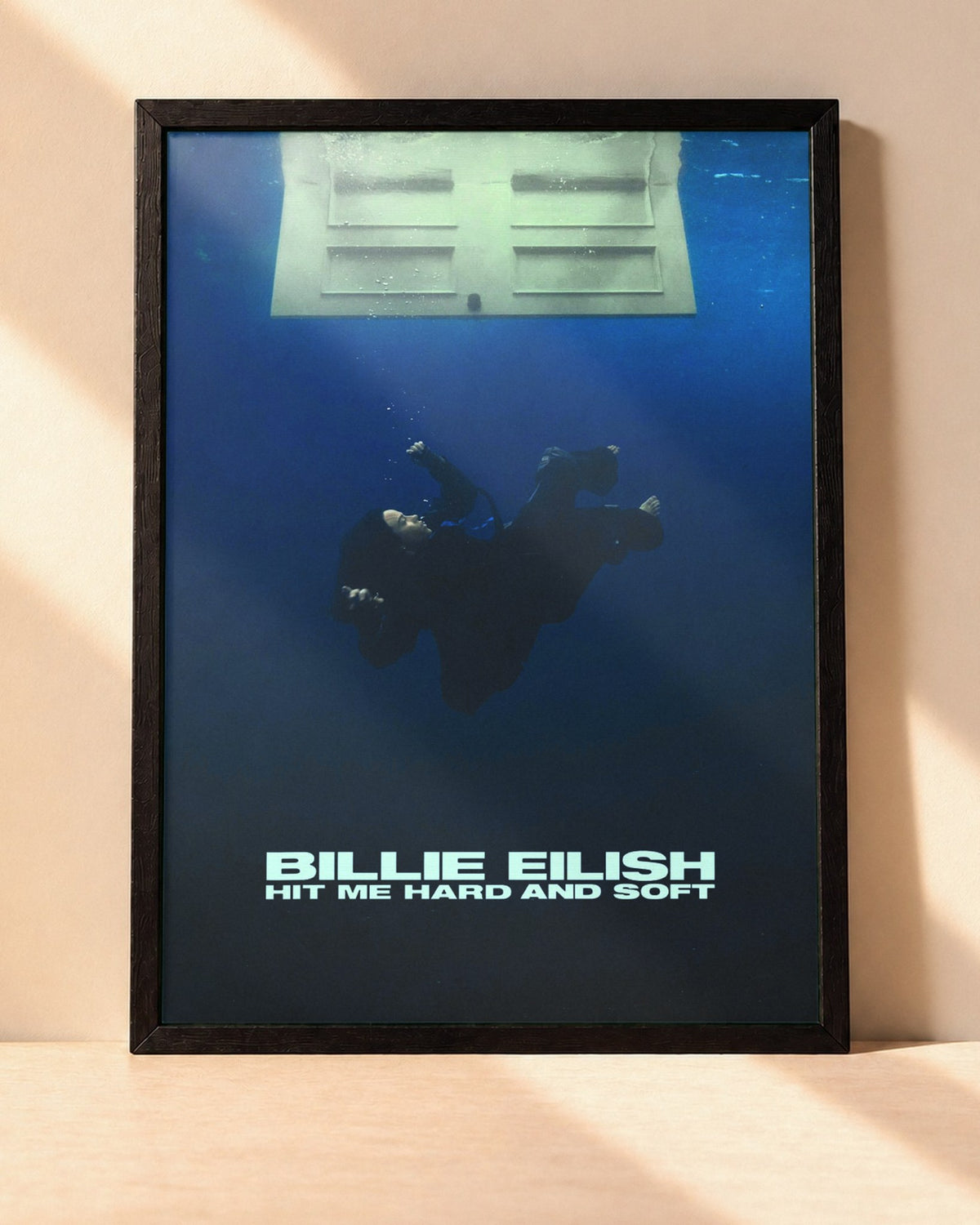 Poster Billie Eilish – Hit Me Hard And Soft encadré dans un cadre noir, posé contre un mur clair