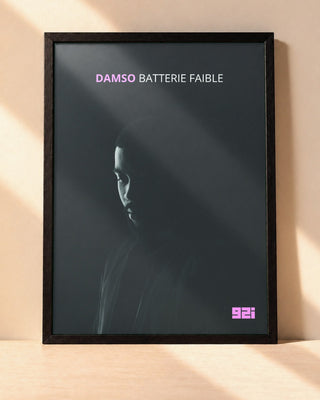 Poster Damso – Batterie Faible encadré dans un cadre noir, posé contre un mur clair