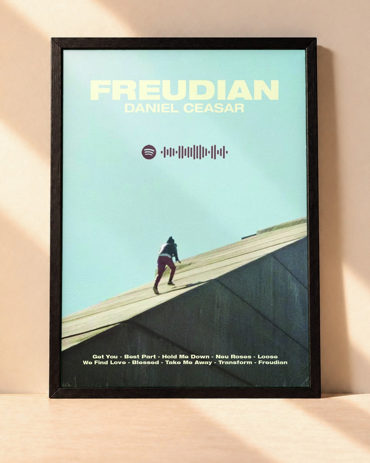Poster Daniel Caesar – Freudian encadré dans un cadre noir, posé contre un mur clair