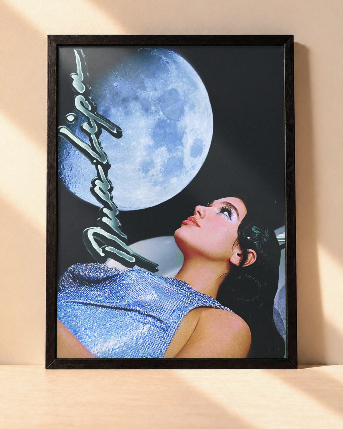 Poster Dua Lipa – Nostalgia encadré dans un cadre noir, posé contre un mur clair
