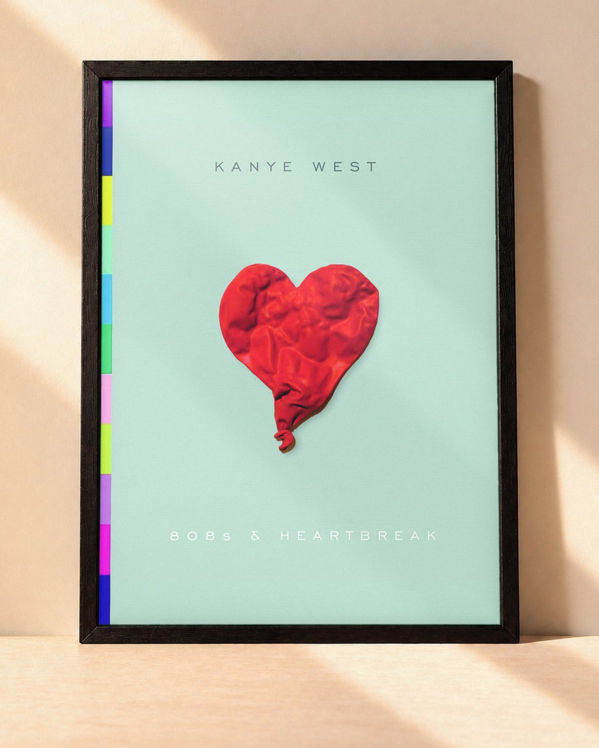Poster Kanye West – 808s & Heartbreak encadré dans un cadre noir, posé contre un mur clair
