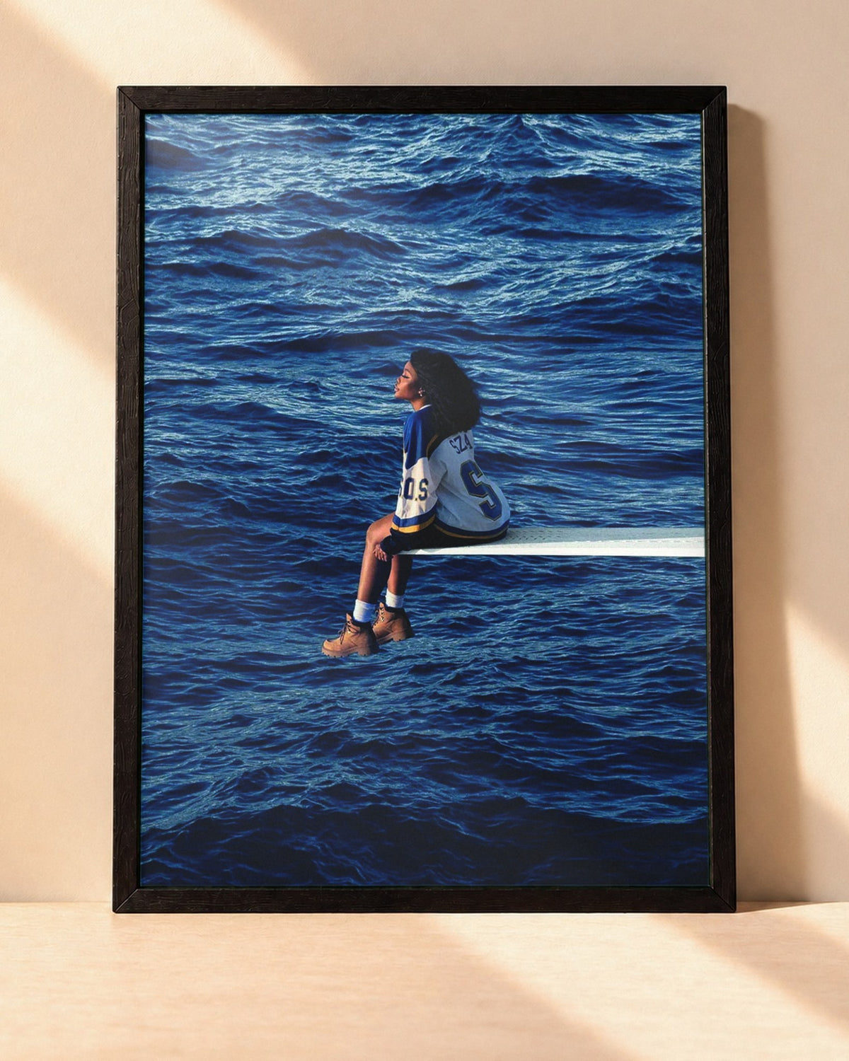 Poster SZA – SOS encadré dans un cadre noir, posé contre un mur clair